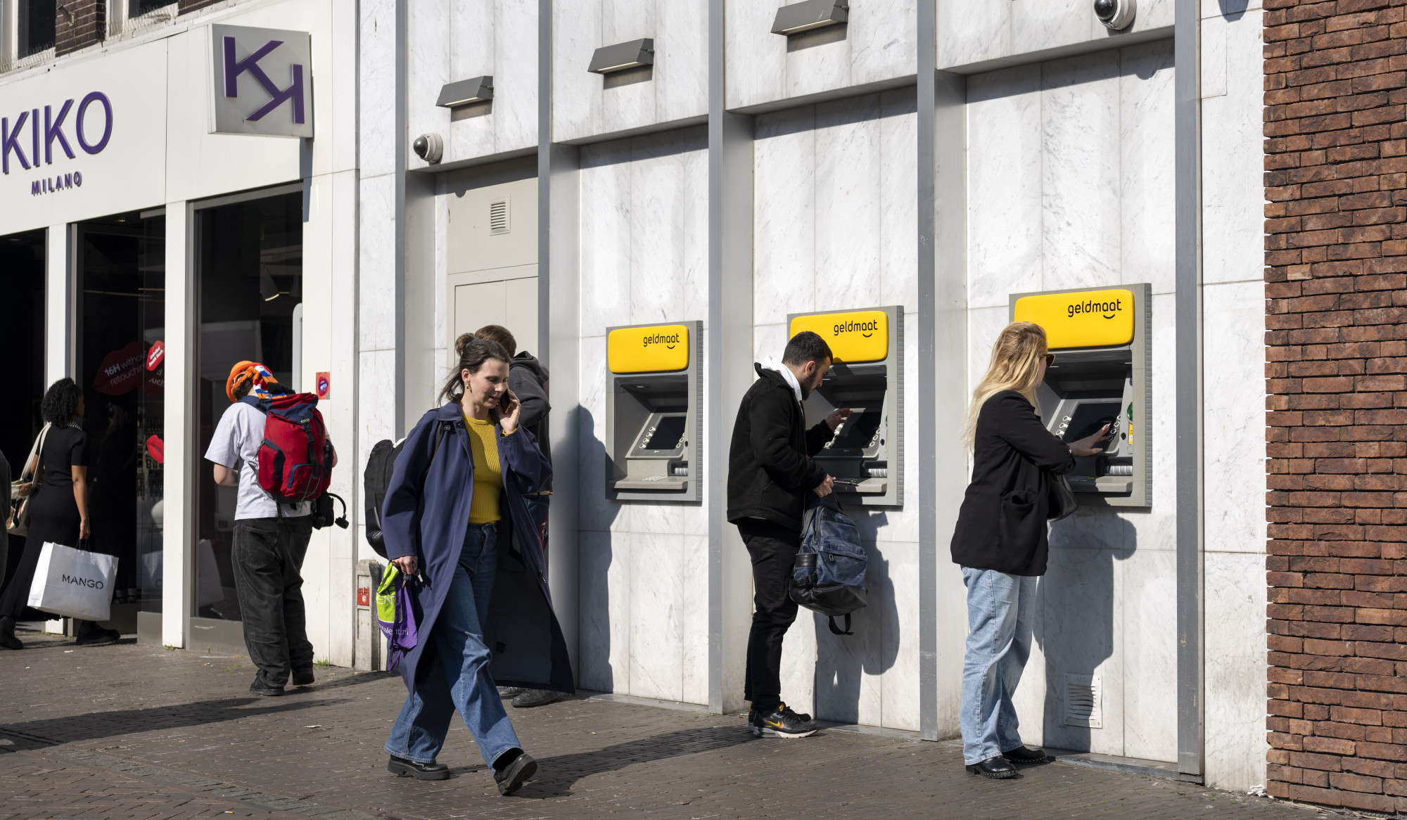 Twee mensen bij rij pinautomaten en voorbijgangers.jpg